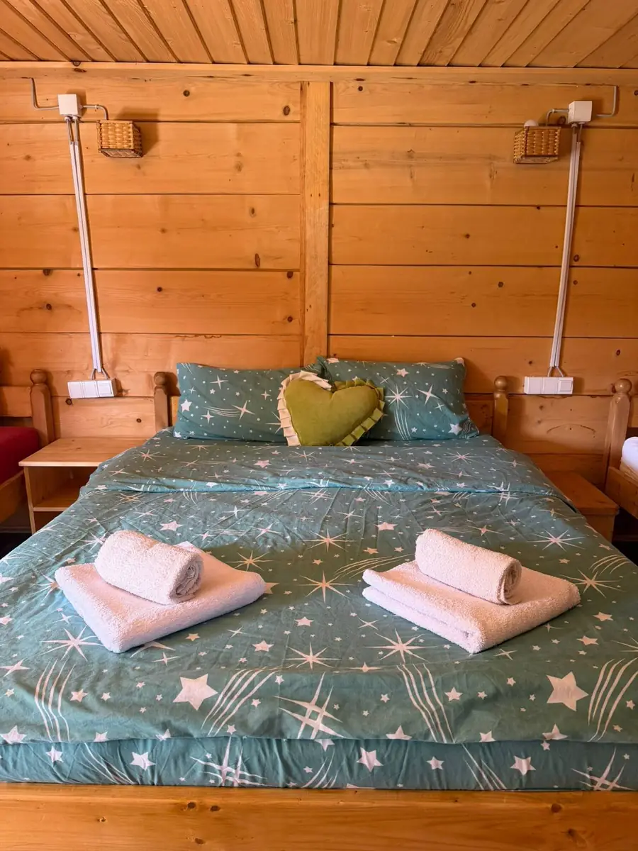 Soba sa francuskim ležajem i zelenom posteljinom u drvenoj vikendici